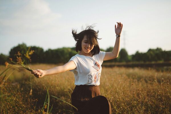 Jeune femme dansant joyeusement dans un champ avec un bouquet de fleurs fraîchement cueillies à la main