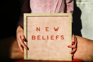 Jeune femme aux ongles vernis rouges tenant un cadre avec l'inscription "New Beliefs" en lettrage rouge