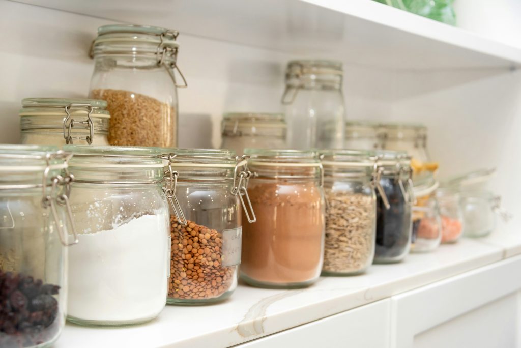 Plusieurs bocaux remplis d'aliments secs bruts alignés sur une étagère en pierre polie blanche. Évocateur d'un garde-manger minimaliste et sain suggérant l'idée que manger varié ne signifie pas nécessairement manger de tout