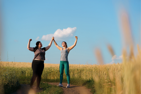 Deux femmes se tiennent la main et lèvent les bras en signe de victoire dans un champ, symbolisant la motivation dans le fait de perdre du poids durablement durable.