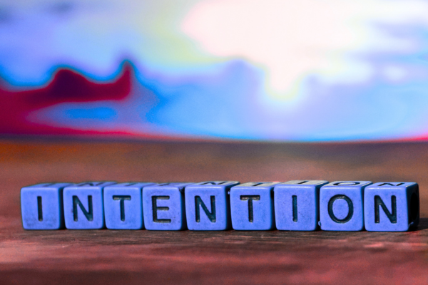 Bloc de lettres formant le mot « intention » posé sur une surface en bois, avec un arrière-plan coloré légèrement flou. Utilisé pour illustrer l'article Le pouvoir de l'intention et ses effets sur la santé