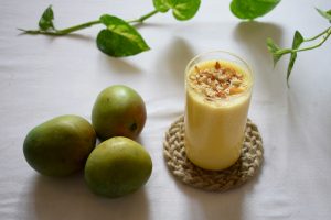Verre de smoothie jaune à base de fruits, garni d’amandes, posé sur un sous-verre, avec des mangues fraîches à côté. Photo utilisée pour illustrer l'article Les faux-amis de l’alimentation saine