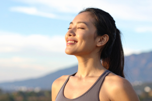 Femme souriante respirant profondément en plein air, les yeux fermés, illustrant une respiration calme et consciente. Photo utilisée pour illustrer l'article du blogue RE:Santé intitulé "Comment la respiration influence notre bien-être, bien au-delà de ce qu’on imagine"