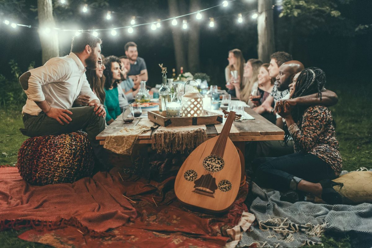 Groupe d’amis partageant un repas convivial à l’extérieur sous des guirlandes lumineuses, illustrant le rôle positif de l’entourage sur la santé et le bien-être. Photo utilisée pour illustrer l'article intitulé "Explore comment ton entourage influence ta santé"