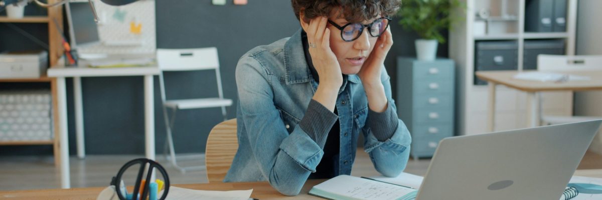 Femme assise devant son ordinateur, visiblement fatiguée, la tête entre les mains, illustrant les effets de la sédentarité et du télétravail prolongé. Utilisée pour illustrer l'article sur les dégâts invisibles de la sédentarité sur la santé