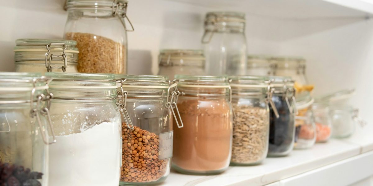 Plusieurs bocaux remplis d'aliments secs bruts alignés sur une étagère en pierre polie blanche. Évocateur d'un garde-manger minimaliste et sain suggérant l'idée que manger varié ne signifie pas nécessairement manger de tout