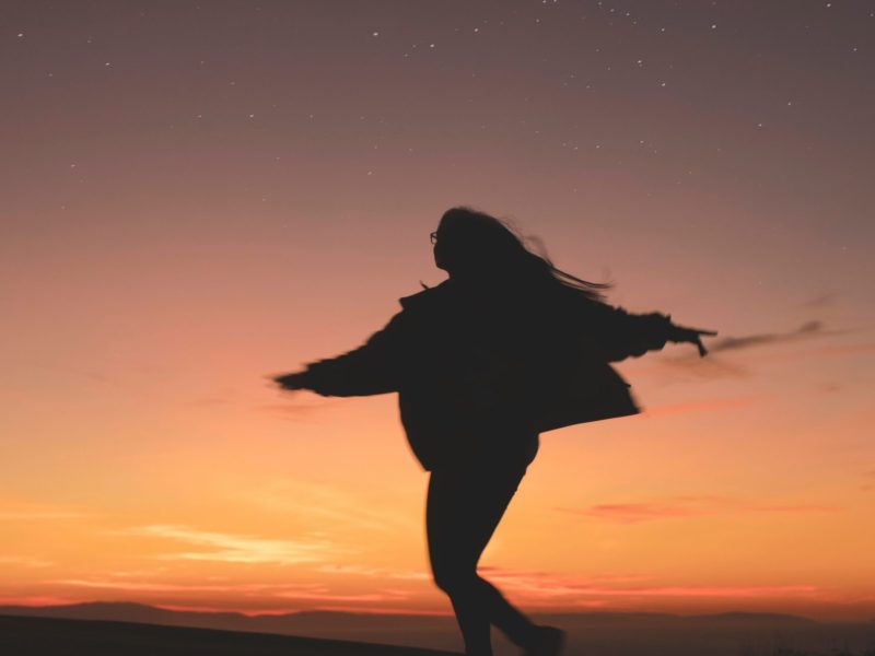 Silhouette d’une femme dansant librement sous un ciel étoilé au crépuscule