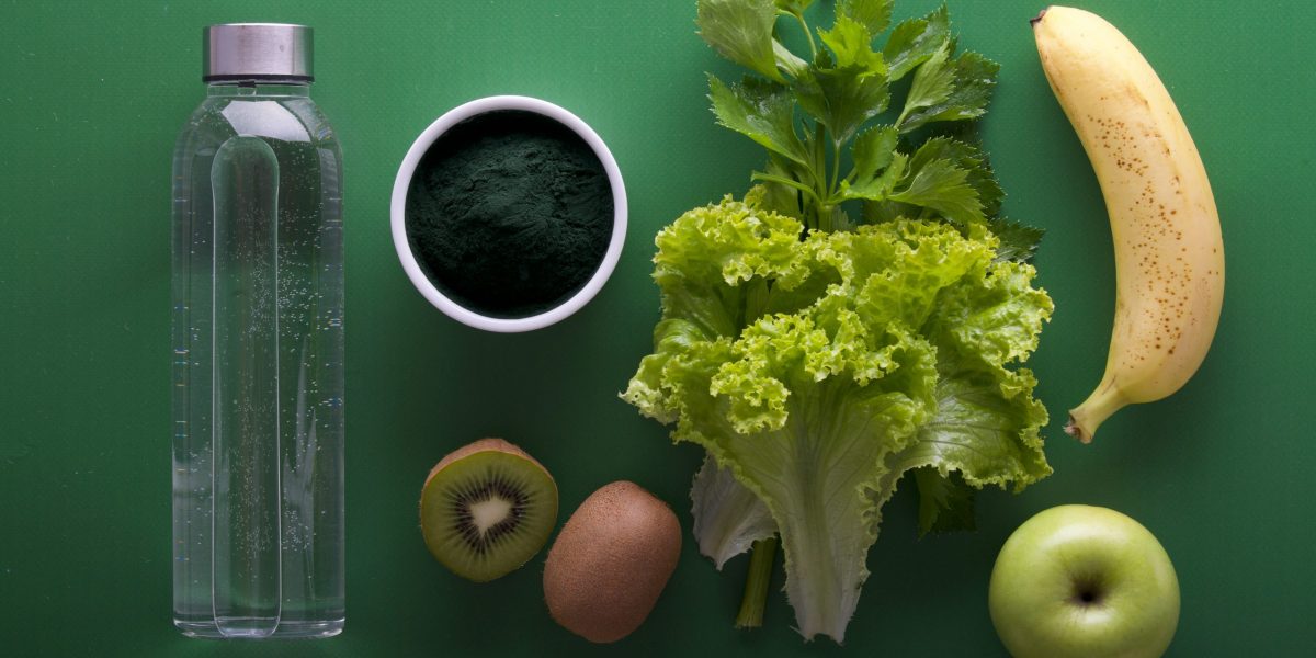Bouteille d’eau, kiwi, pomme verte, banane, laitue et poudre verte sur fond vert – aliments frais pour une alimentation saine et détox
